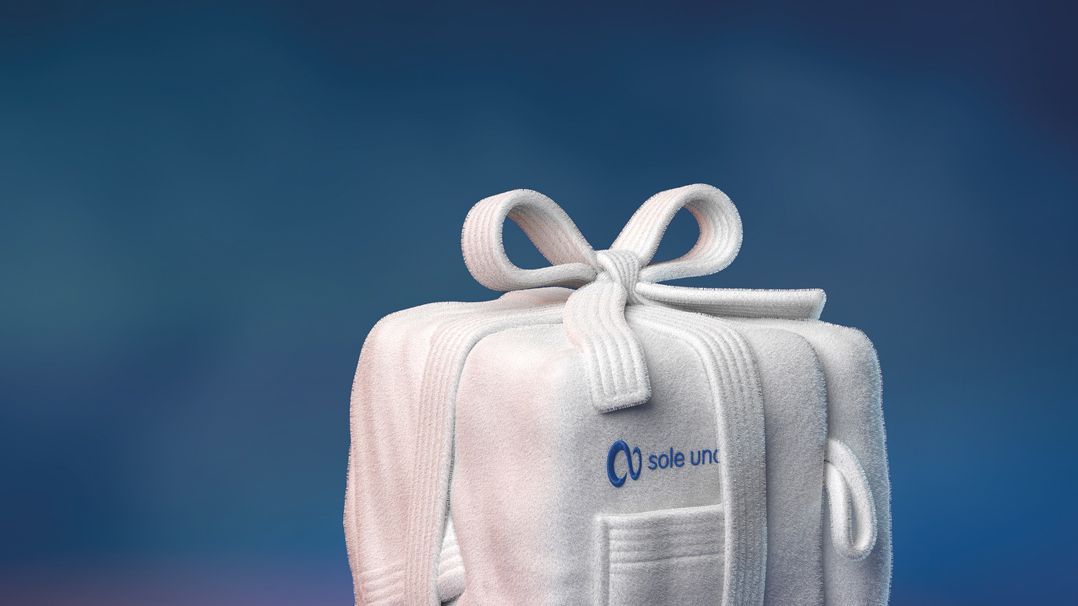 Weihnachtlich verpacktes Wellness-Geschenk mit dem Logo von sole uno auf einer weichen, weißen Frottier-Tasche vor blau-violettem Hintergrund.