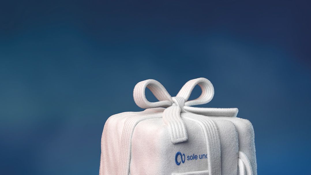 Weihnachtlich verpacktes Wellness-Geschenk mit dem Logo von sole uno auf einer weichen, weißen Frottier-Tasche vor blau-violettem Hintergrund.