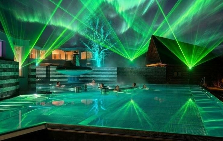 Gruene Laserstrahlen und Polarlicht-Effekte ueber dem beleuchteten Aussenbecken der Wellness-Welt sole uno in Rheinfelden.