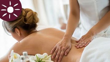 A woman is lying on her stomach on a massage table and is receiving a back massage from a massage therapist.