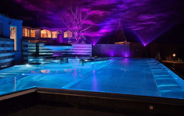Beleuchtetes Aussenbecken der Wellnesswelt sole uno in Rheinfelden bei Nacht mit violetter Lichtinstallation und Lichtershow.