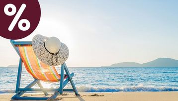 Gestreifter Liegestuhl mit Sonnenhut an einem hellen Sandstrand vor blauem Meer – Symbolbild für den sole uno Monats-Hit „Ein Tag am Meer“.