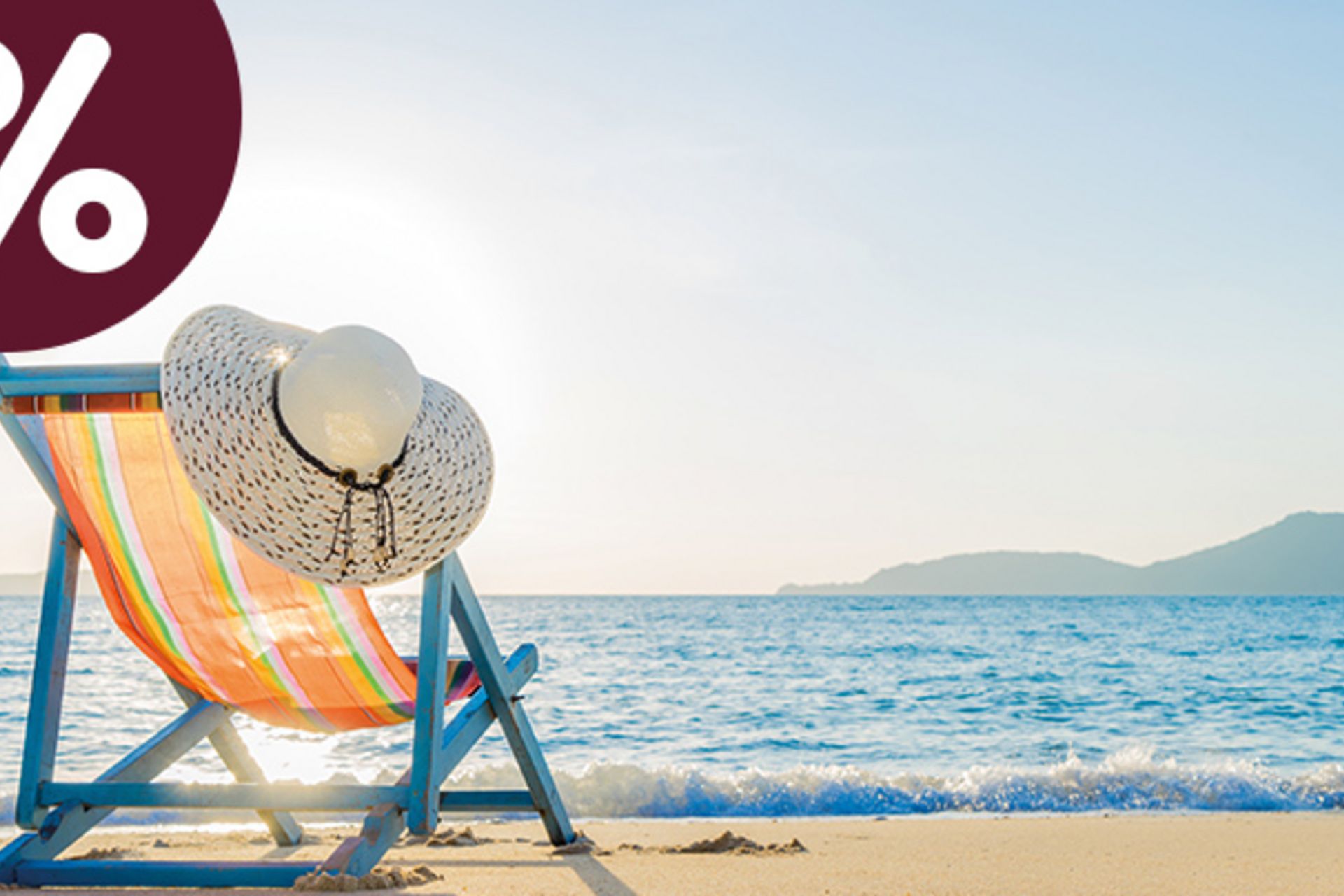 Gestreifter Liegestuhl mit Sonnenhut an einem hellen Sandstrand vor blauem Meer – Symbolbild für den sole uno Monats-Hit „Ein Tag am Meer“.